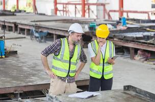 Caucasian engineer and female foreman worker with blueprints checking project at the precast concrete factory site, Engineer team in hardhats discussing on construction site photo
