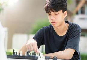 Asian teenage boy playing chess board, Asian boy relaxing hobbies playing a game of chess outdoor photo