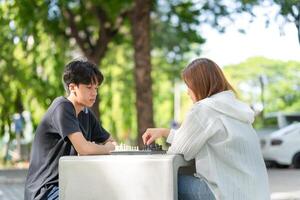 Mother playing chess with a son, Asian family relaxing hobbies playing chess in a park photo
