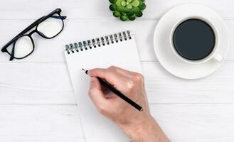 A man's hand writes something with a pencil in a notepad. Workplace. Top view. Flatlay. Selective focus. photo