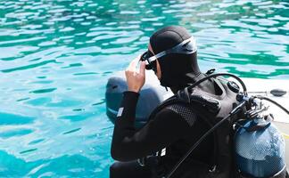 A diver in a wetsuit and mask with a scuba is about to dive into the water from a boat. Diving lessons. Close-up. Copy space. photo