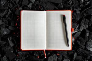 An open checkered notebook lying on a dark charcoal with red flashes of heat. photo