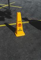 Yellow road cone with a warning not to park on a back of gray asphalt road. photo
