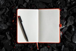 An open checkered notebook lying on a dark charcoal with red flashes of heat. photo