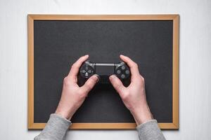 Hands hold new joystick on blackboard. Gamer play game with gamepad controller. photo
