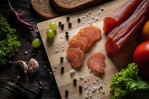 Sliced jerky on a board. Vegetables, bread and meat on the table. photo