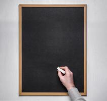 Male hand with chalk on the empty blackboard or chalkboard. photo