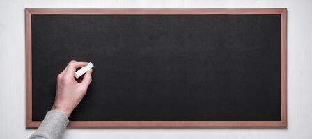 Hand holding chalk on blackboard. Male hand with chalk on the empty blackboard or chalkboard. photo