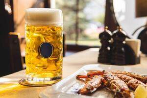 Big mug of fresh cold beer and fried tiger prawns on the table. A low-alcohol beverage and a snack are on the table. Light back. photo