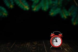 Red alarm clock on a dark wooden background with fir branches. Five to twelve on the clock. Christmas card, blank. photo