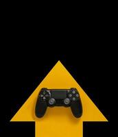 Modern black gamepad on a yellow arrow on a black background. Joystick on a yellow direction indicator on a dark background. Flat lay copyspace. photo