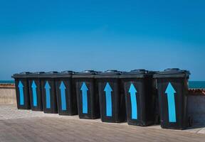 Black plastic garbage cans near the sea. Containers for different rubbish on a background of blue sky. Garbage sorting for further processing. photo