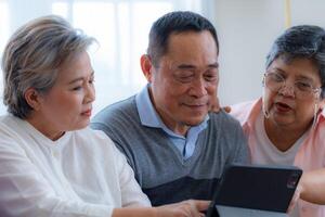 Happiness of the group females and male elderly talking with Call from smart tablet. Senior people are talking and enjoy together at the living room. Joyful retired friends enjoying relaxation. photo