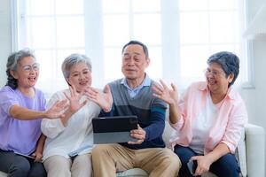 Happiness of the group females and male elderly talking with Call from smart tablet. Senior people are talking and enjoy together at the living room. Joyful retired friends enjoying relaxation. photo
