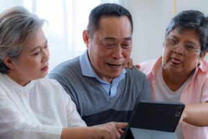 Happiness of the group females and male elderly talking with Call from smart tablet. Senior people are talking and enjoy together at the living room. Joyful retired friends enjoying relaxation. photo