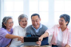 Happiness of the group females and male elderly talking with Call from smart tablet. Senior people are talking and enjoy together at the living room. Joyful retired friends enjoying relaxation. photo
