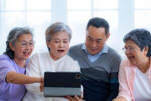 Happiness of the group females and male elderly talking with Call from smart tablet. Senior people are talking and enjoy together at the living room. Joyful retired friends enjoying relaxation. photo