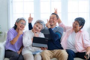 Happiness of the group females and male elderly talking with Call from smart tablet. Senior people are talking and enjoy together at the living room. Joyful retired friends enjoying relaxation. photo