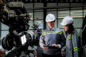 team engineers inspecting on machine with smart tablet. Worker works at heavy machine robot arm. The welding machine with a remote system in an industrial factory. Artificial intelligence concept. photo