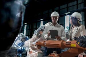 team engineers inspecting on machine with smart tablet. Worker works at heavy machine robot arm. The welding machine with a remote system in an industrial factory. Artificial intelligence concept. photo