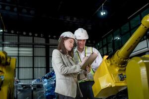 team engineers inspecting on machine with smart tablet. Worker works at heavy machine robot arm. The welding machine with a remote system in an industrial factory. Artificial intelligence concept. photo