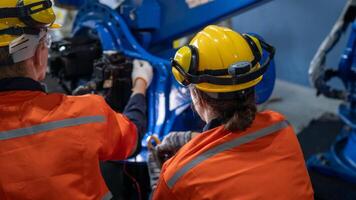 group of male engineer workers maintenance automatic robotic arm machine in a dark room factory. worker checking and repairing automatic robot hand machine. Worker wearing safety glasses and helmet. photo