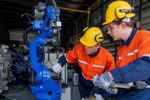group of male engineer workers maintenance automatic robotic arm machine in a dark room factory. worker checking and repairing automatic robot hand machine. Worker wearing safety glasses and helmet. photo