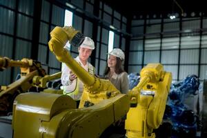 team engineers inspecting on machine with smart tablet. Worker works at heavy machine robot arm. The welding machine with a remote system in an industrial factory. Artificial intelligence concept. photo