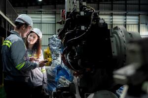 team engineers inspecting on machine with smart tablet. Worker works at heavy machine robot arm. The welding machine with a remote system in an industrial factory. Artificial intelligence concept. photo