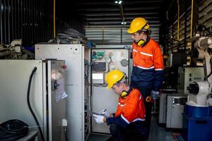group of male engineer workers maintenance automatic robotic arm machine in a dark room factory. worker checking and repairing automatic robot hand machine. Worker wearing safety glasses and helmet. photo