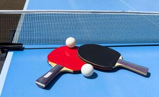 Two table tennis rackets and balls on a blue table with net. photo