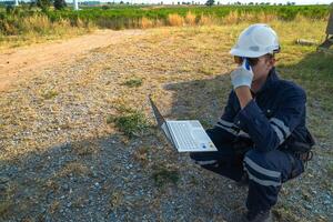 A technician in safety gear meticulously records data with a wind turbine in the backdrop at dusk. photo