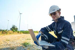A technician in safety gear meticulously records data with a wind turbine in the backdrop at dusk. photo