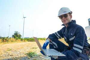 A technician in safety gear meticulously records data with a wind turbine in the backdrop at dusk. photo