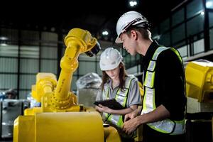 team engineers inspecting on machine with smart tablet. Worker works at heavy machine robot arm. The welding machine with a remote system in an industrial factory. Artificial intelligence concept. photo