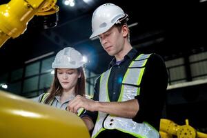 team engineers inspecting on machine with smart tablet. Worker works at heavy machine robot arm. The welding machine with a remote system in an industrial factory. Artificial intelligence concept. photo