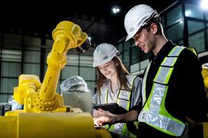 team engineers inspecting on machine with smart tablet. Worker works at heavy machine robot arm. The welding machine with a remote system in an industrial factory. Artificial intelligence concept. photo