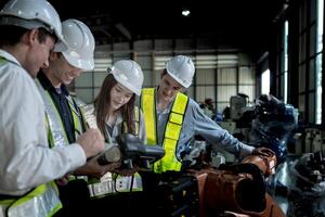 team engineers inspecting on machine with smart tablet. Worker works at heavy machine robot arm. The welding machine with a remote system in an industrial factory. Artificial intelligence concept. photo