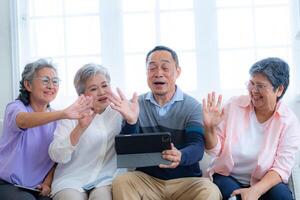 Happiness of the group females and male elderly talking with Call from smart tablet. Senior people are talking and enjoy together at the living room. Joyful retired friends enjoying relaxation. photo