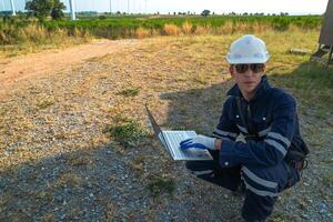 A technician in safety gear meticulously records data with a wind turbine in the backdrop at dusk. photo