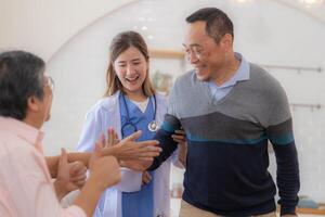 Asian young nurse support senior older man walk with walker. Beautiful nurse help and take care. elderly mature grandpa patient doing physical therapy with a group of senior friends in hospital. photo