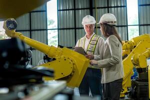 team engineers inspecting on machine with smart tablet. Worker works at heavy machine robot arm. The welding machine with a remote system in an industrial factory. Artificial intelligence concept. photo