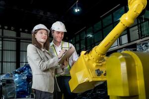 team engineers inspecting on machine with smart tablet. Worker works at heavy machine robot arm. The welding machine with a remote system in an industrial factory. Artificial intelligence concept. photo