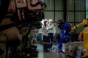 team engineers inspecting on machine with smart tablet. Worker works at heavy machine robot arm. The welding machine with a remote system in an industrial factory. Artificial intelligence concept. photo