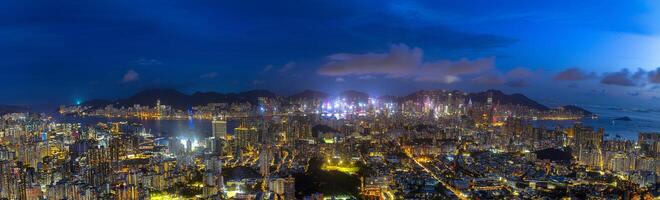 Hong Kong city view from above with modern buildings and towns lit up at night across island. Light hits buildings which creating focal point in city with modern buildings and road with traffic light. photo