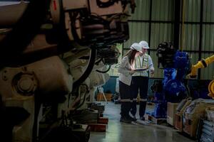 team engineers inspecting on machine with smart tablet. Worker works at heavy machine robot arm. The welding machine with a remote system in an industrial factory. Artificial intelligence concept. photo