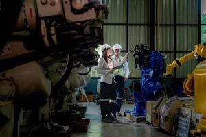 team engineers inspecting on machine with smart tablet. Worker works at heavy machine robot arm. The welding machine with a remote system in an industrial factory. Artificial intelligence concept. photo