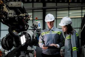 team engineers inspecting on machine with smart tablet. Worker works at heavy machine robot arm. The welding machine with a remote system in an industrial factory. Artificial intelligence concept. photo