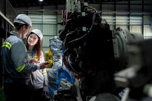 team engineers inspecting on machine with smart tablet. Worker works at heavy machine robot arm. The welding machine with a remote system in an industrial factory. Artificial intelligence concept. photo