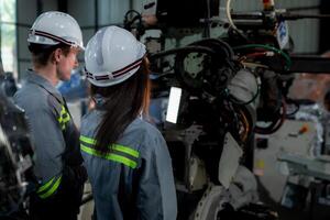 team engineers inspecting on machine with smart tablet. Worker works at heavy machine robot arm. The welding machine with a remote system in an industrial factory. Artificial intelligence concept. photo